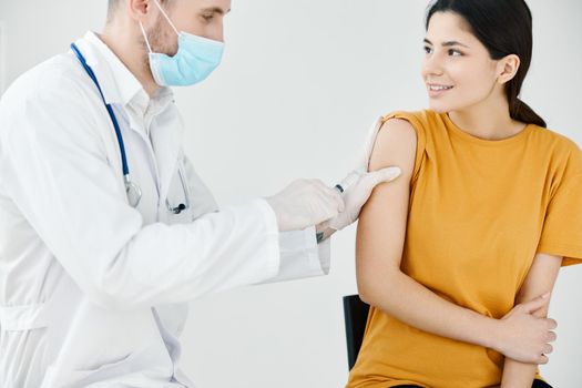 a doctor in a medical mask and a dressing gown seals an injection on a woman's shoulder with adhesive plaster. High quality photo