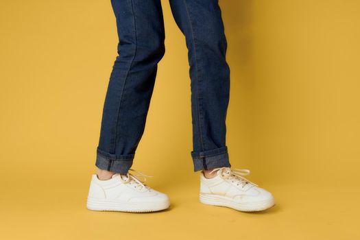 Fashionable shoes white sneakers legs yellow background cropped view. High quality photo