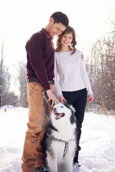 Young couple with siberian husky dog in winter in the park.