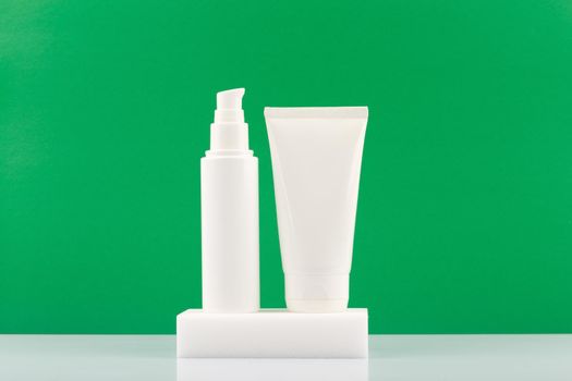 White cosmetic tubes on white podium against green background with copy space. Face and hands cream, lotion, mask or scrub. Concept of organic skin care products with natural ingredients and oils