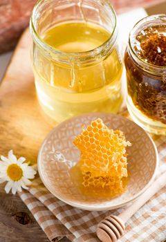 Close up honeycomb with honey in glass jar on wooden board, top view