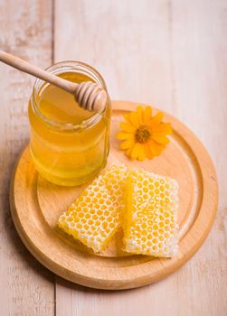 Honey dipper on the bee honeycomb background. Honey tidbit in glass jar and honeycombs.