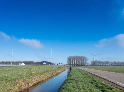 country road with meadow and trees near motorway A27 and A2 in the netherlands under blue sky near Vianen and Utrecht in the netherlands