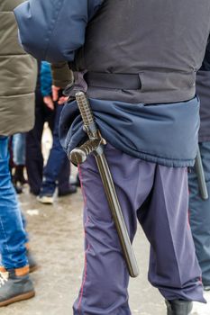 russian police officer with black rubber tonfa baton sticking out from uniform, close-up with selective focus
