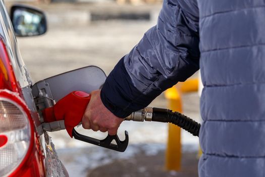 old man hand in blue warm jacket refueling gray metallic car on gas station at day time - close-up with selective focus and background blur