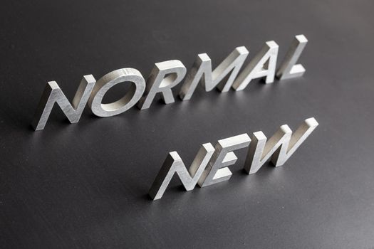 new normal word composed of silver metal letters on a flat matt black surface with diagonal perspective.