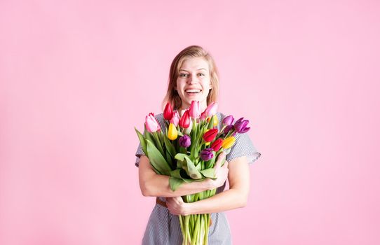 Women's Day or Mother's Day celebration. Happy young woman holding bouquet of fresh tulips isolated on pink background