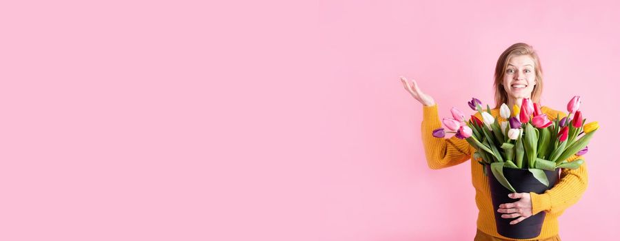 Women's Day or Mother's Day celebration. Banner. Happy young woman holding bucket of fresh tulips isolated on pink background