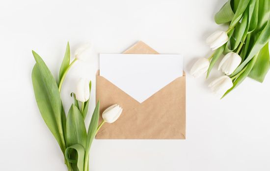 Mock up design. Fresh cut white tulip flowers and blank card with envelope top view on white background with copy space