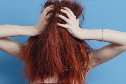 red-haired woman touching her head with hands emotions tousled hair blue background. High quality photo