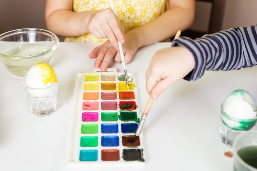 Close-up on the hands of little Caucasian children who paint eggs with special paints for the Christian spring holiday of Easter.