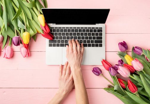 Easter and spring concept. Woman hands typing on laptop keyboard. Feminime worlspace decorated with tulips