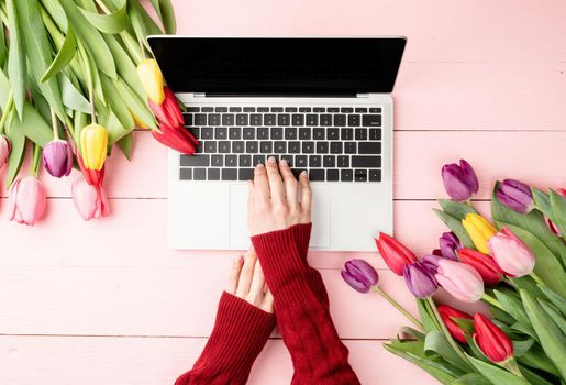 Easter and spring concept. Woman hands typing on laptop keyboard. Feminime worlspace decorated with tulips