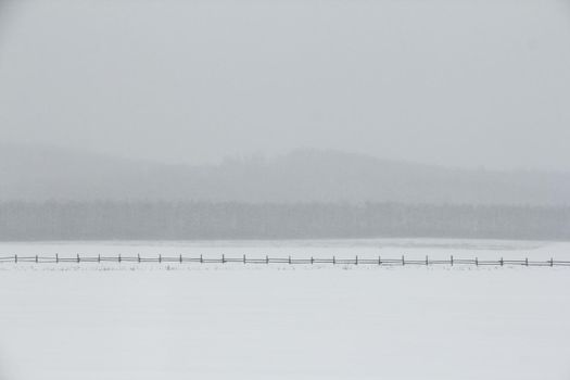 Minimalistic winter landscape with fresh snow, fog and haze among mountains, old fence