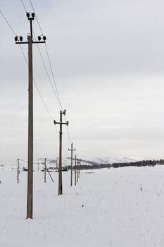 Row of wooden electric poles on empty hilly snow covered landscape. Electrical industry, power line, wiring.