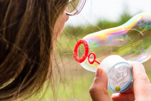 Close up photo of a girl blowing soap bubbles outdoor.