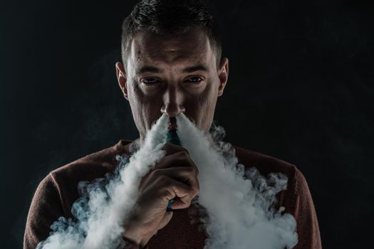 a man smokes a vape on a black background white smoke steam portrait close-up. High quality photo