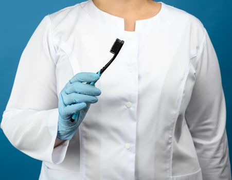 woman doctor in a white medical coat and mask stands on a blue background and holds a plastic toothbrush, close up