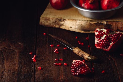 Pomegranate fruits with knife on rustic wooden surface.