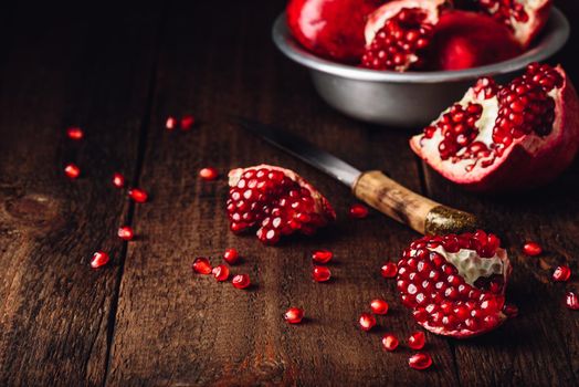 Pomegranate fruits with knife on rustic wooden surface.