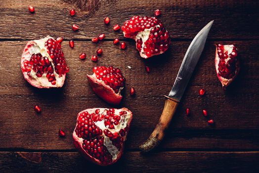 Pomegranate pieces with knife on rustic wooden surface. View from above