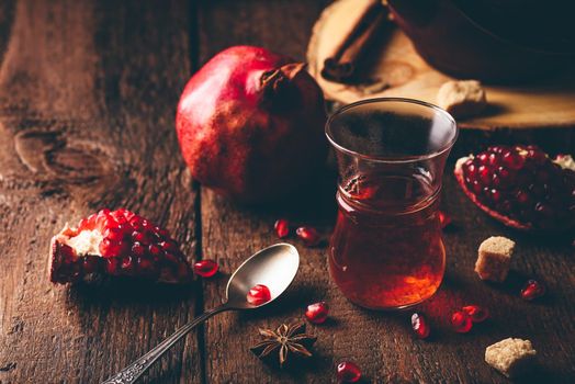 Black tea in arabic tea glass with fresh pomegranate and some spices on wooden table