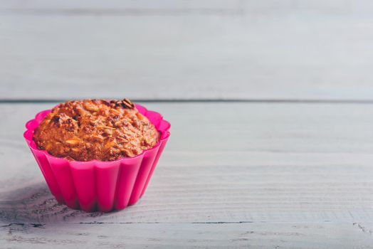 Cooked oatmeal muffin in a pink silicone bakeware over light wooden background.