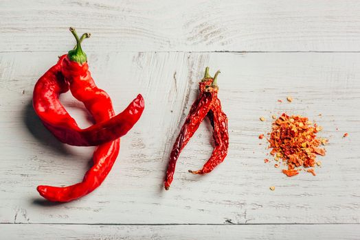 Fresh, dried and crushed red chili pepper over colored wooden background