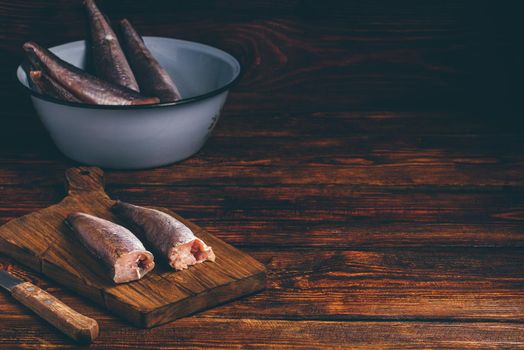 Hake carcasses on cutting board with knife and bowl over wooden surface