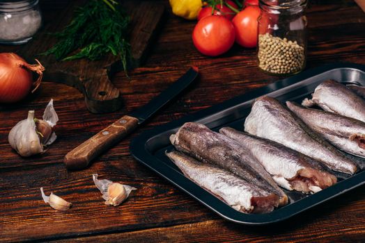 Hake carcasses on baking sheet with vegetables and spices