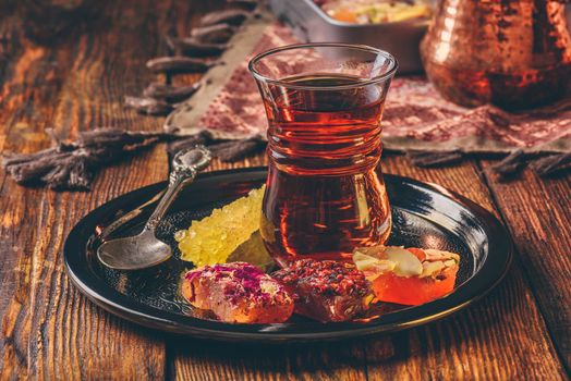 Tea in armudu glass with oriental delight rahat lokum on metal tray over wooden surface and tablecloth