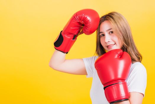 Portrait Asian Thai beautiful young woman standing smile wearing red boxing gloves she poses like a boxer, studio shot isolated on yellow background, There was copy space for text