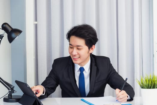 Work from home, Asian young businessman video conference call or facetime he smiling looking to tablet sitting on desk using smart digital tablet computer touching on screen at home office