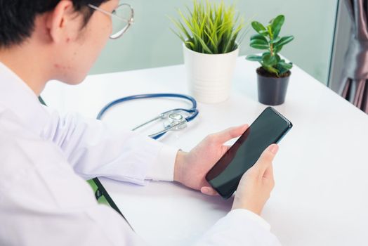 Asian doctor young handsome man smiling using working or holding with digital smart mobile phone at hospital desk office, Technology healthcare medical concept