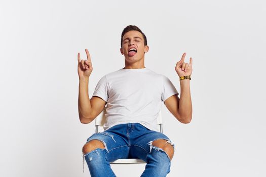 Man on a chair indoors torn jeans white t-shirt handsome face model light background. High quality photo