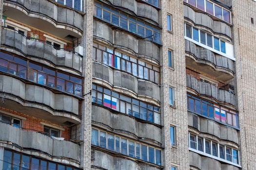 old dirty large russian apartment building balcony windows with russian tricolor flags