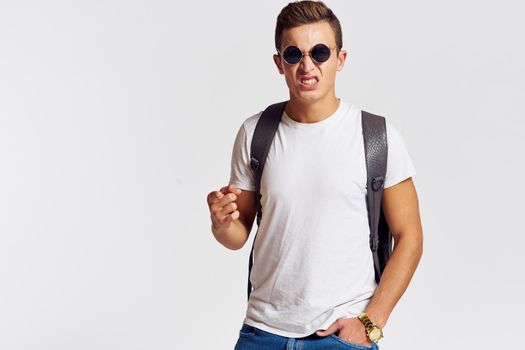 man in sunglasses with a backpack on his back and in a white t-shirt on a light background cropped view of emotion. High quality photo