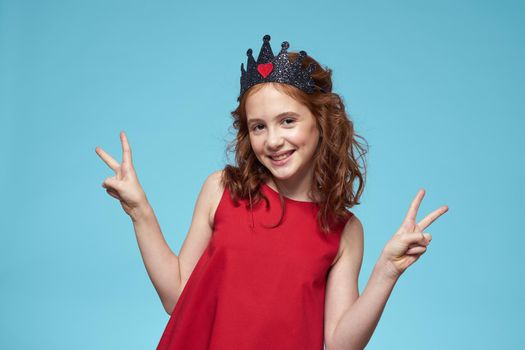 Girl with curly hair with a crown on her head red dress lifestyle blue background. High quality photo