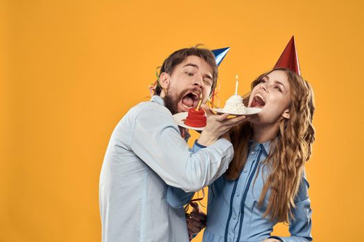 Energetic man and pretty woman with birthday cake in hats on a yellow background disco party. High quality photo