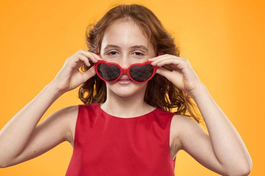 Girl in black glasses red dress childhood fun yellow background. High quality photo