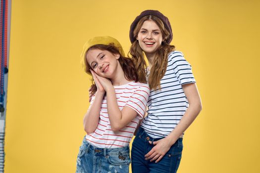 Cheerful sisters in hats striped T-shirts joy lifestyle yellow background family. High quality photo