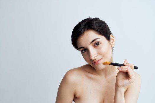 Pretty woman with naked shoulders applying makeup on face lifestyle. High quality photo