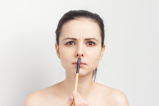 cute bare-shouldered brunette applying makeup on face cropped view. High quality photo
