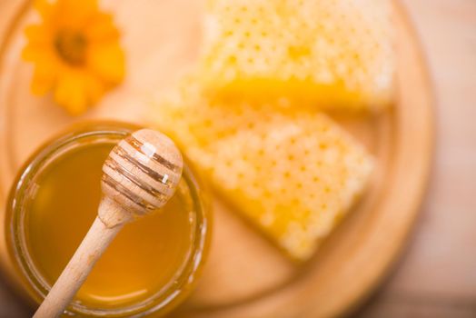 Honey dipper on the bee honeycomb background. Honey tidbit in glass jar and honeycombs.