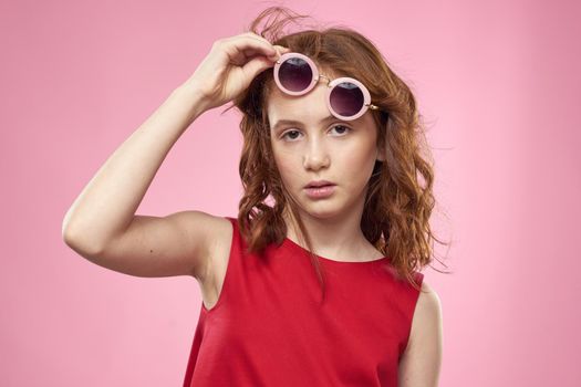 Girl with curly hair dark round glasses fun red dress pink background. High quality photo