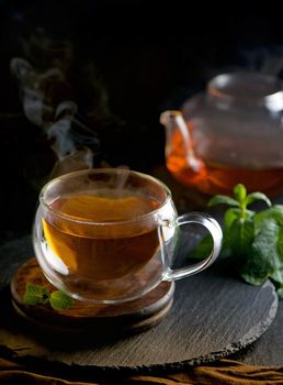 Teapot with tea surrounded with green leaves, tea ceremony, green tea in a transparent cup