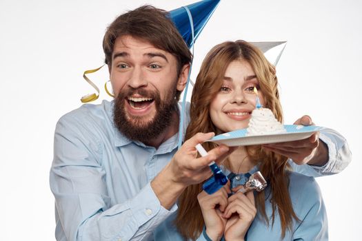 energetic man and woman with a cake and in hats celebrate a birthday on a light background. High quality photo