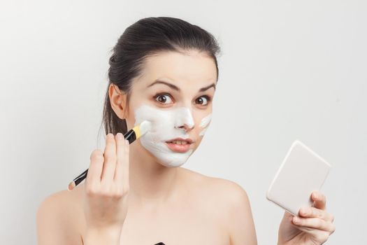 cute bare-shouldered brunette applying makeup on face cropped view. High quality photo