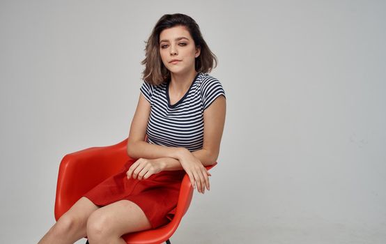 fashionable woman in a striped t-shirt sits on a red chair In a bright room Copy Space. High quality photo