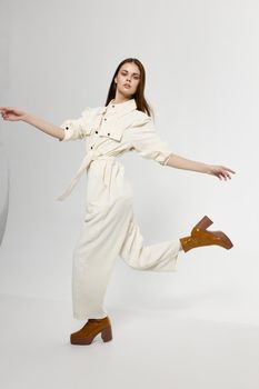fashionable woman in white jumpsuit runs to the side in boots and gestures with her hands. High quality photo